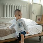 A small child exploring a modern bedroom, stepping on a woven ottoman.
